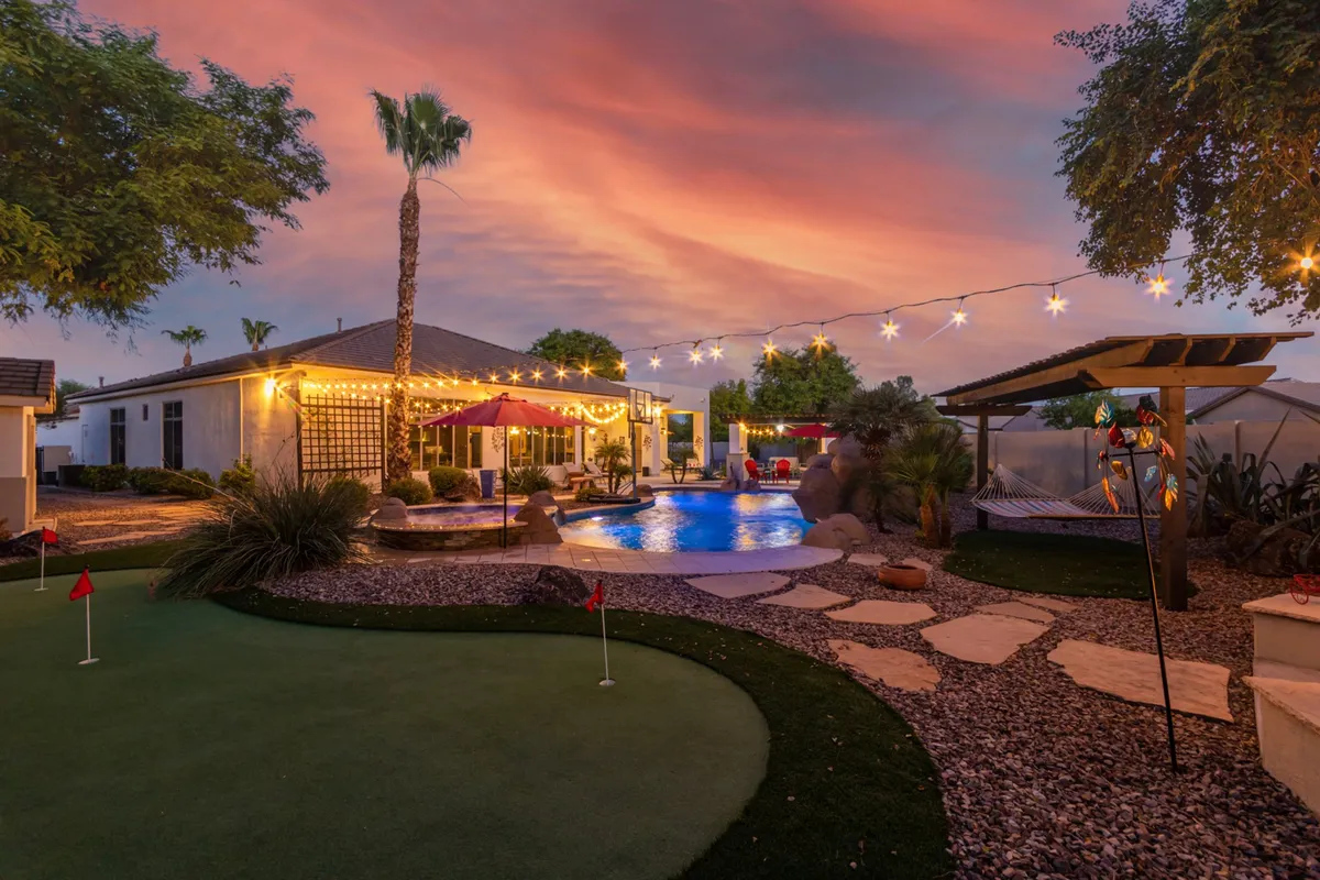 Featuring a vibrant backyard with a swimming pool, outdoor seating, putting green, and string lights, this image captures a lively space perfect for both friendly golf practice and social gatherings. The sunset glow and festive lighting reinforce an atmosphere of celebration and outdoor enjoyment.