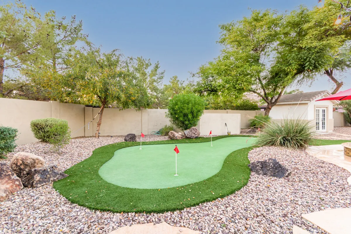 A lively exterior view of a backyard putting green surrounded by decorative rocks and lush greenery. The space is designed for both recreation and relaxation, with ample room for friendly competitions or unwinding at sunset.