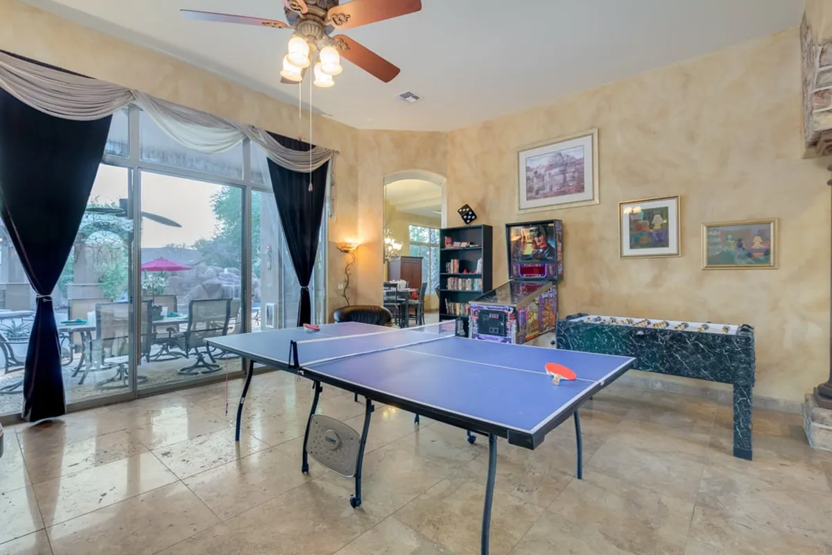 A modern interior scene with a large ping pong table as the focal point, complemented by an entertainment center, black curtains, and stylish wall art. The setup is perfect for energetic game nights, socializing, and hosting informal tournaments.