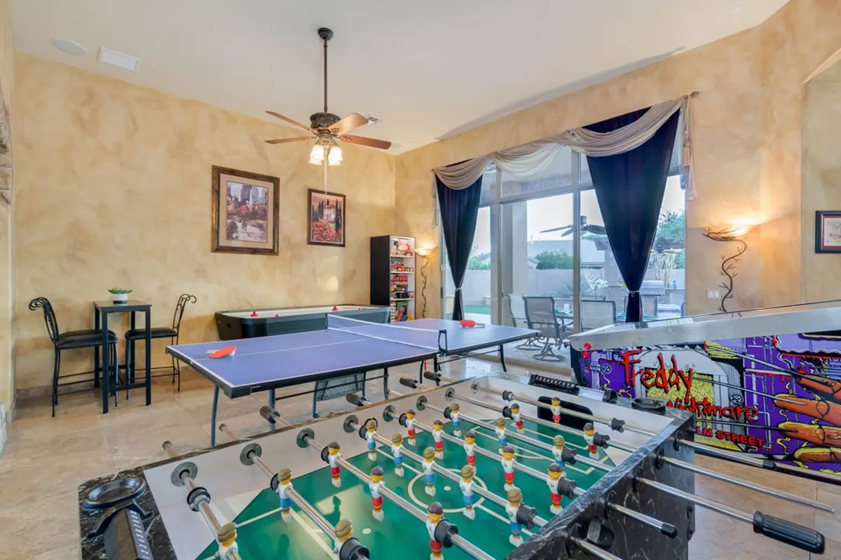 This image presents a vibrant game room, with a foosball table and ping pong table set up for play. There is a small dining table for snacks or board games, decorative wall art that adds to the playful atmosphere, and ample space for guests to gather and compete. The overall energy is lively and welcoming, perfect for families and groups.