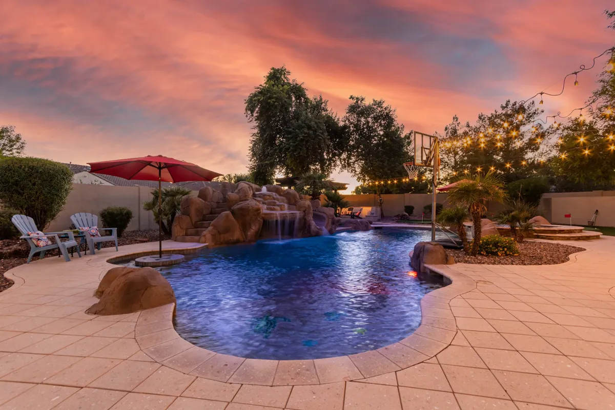 This backyard scene centers on a sparkling swimming pool with a waterfall feature, basketball hoop, and ample lounge chairs under umbrellas. The mood is tranquil yet playful, ideal for unwinding or connecting with family and friends after a day on the golf course.