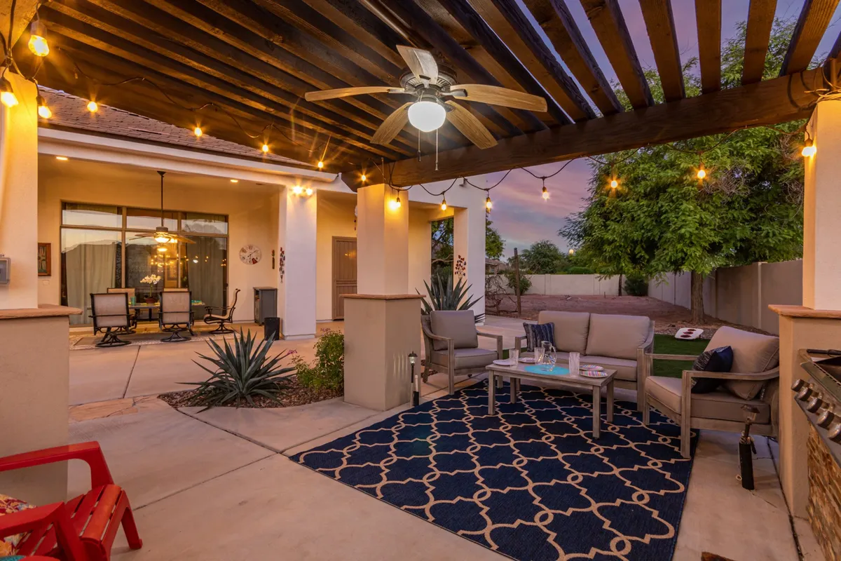 A shaded seating area surrounded by lush plants, illuminated by hanging lights, and featuring a decorative rug. The ambiance is both tranquil and welcoming, providing an inviting spot for relaxing or playing with a pet.