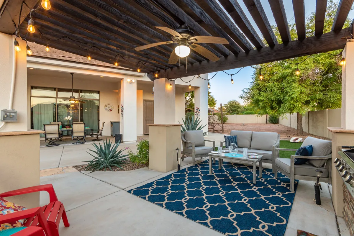 This image features a cozy outdoor seating area adorned with a decorative rug, string lights, and lush potted plants. The setting feels intimate and welcoming, perfect for relaxing with a pet or enjoying quiet moments together outside.