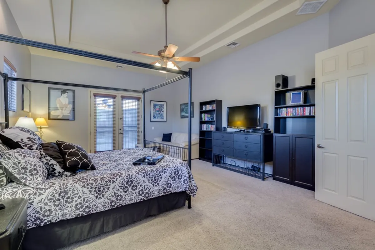 A tranquil bedroom with a four-poster bed, entertainment center, and large windows with blinds. The soft lighting and inviting bed create an atmosphere of peaceful relaxation, ideal for unwinding at the end of the day.